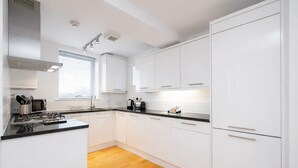 A modern kitchen with white cabinets, a black countertop, and a wooden floor. - Roomspace Apartments -Kew Bridge Court (London)