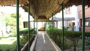 A covered walkway with a tiled floor, green metal columns, and a thatched roof. - Hotel Le Sahel (Maroua)