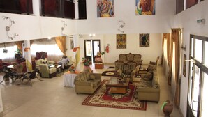 A spacious living area with multiple seating options, including sofas and chairs, arranged around a central coffee table. There are decorative elements like plants and artwork on the walls. - Hotel Le Sahel (Maroua)