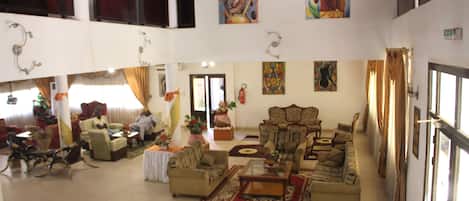 A spacious living area with multiple seating options, including sofas and chairs, arranged around a central coffee table. There are decorative elements like plants and artwork on the walls.