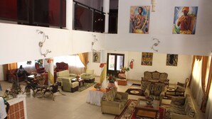 A spacious living area with multiple seating options, including sofas and chairs, arranged around a central coffee table. There are decorative plants and artwork on the walls. - Hotel Le Sahel (Maroua)