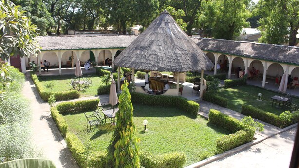 A courtyard with a thatched-roof pavilion, neatly trimmed hedges, and a small water feature. - Hotel Le Sahel (Maroua)