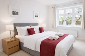 A neatly arranged bedroom with a bed, bedside tables, and a window with curtains.