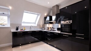 A modern kitchen with black cabinets, stainless steel appliances, and a skylight. - Roomspace Apartments -Kinnaird Court (Esher)