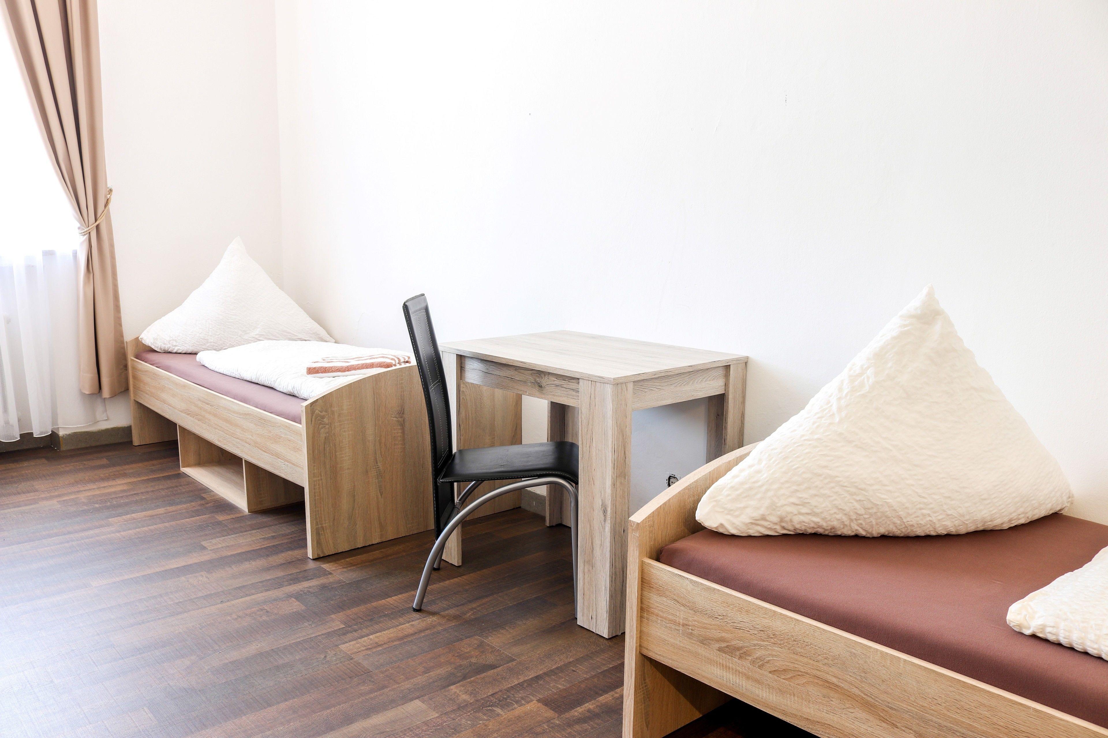 Una habitación con dos camas de madera, un escritorio pequeño y una silla.