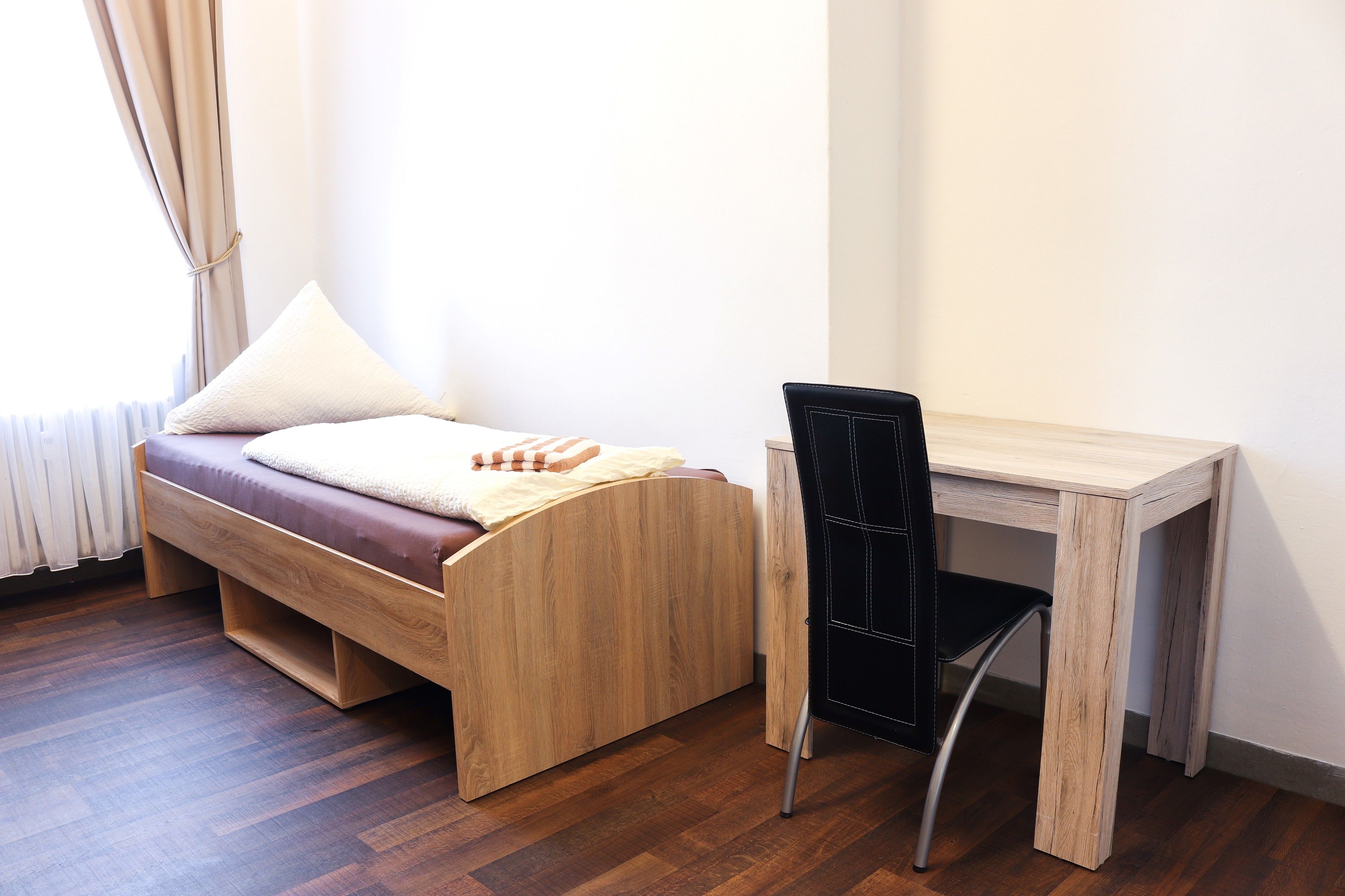 A compact room with a wooden bed, a small desk, and a chair.