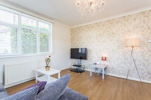 A living room with a TV, a white radiator, a potted plant, and a chandelier. - Leigh Apartments (Southend-on-Sea)