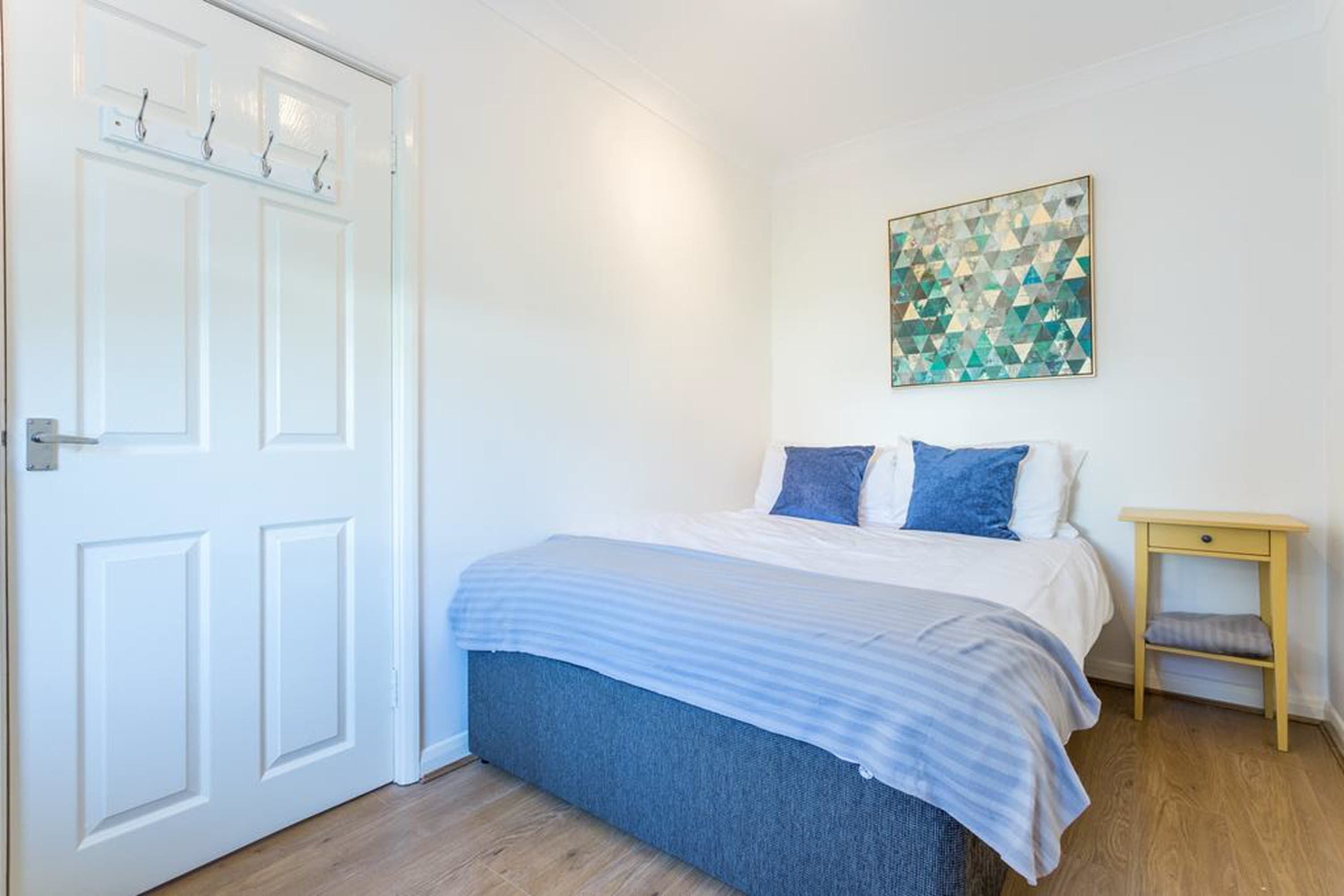 Ein Schlafzimmer mit Bett, Nachttisch, Wandbild und einer Tür.