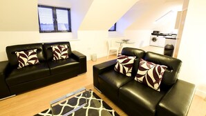 A modern living room with two black leather sofas, patterned cushions, a glass coffee table, and a giraffe-patterned rug. - Roomspace Apartments -Kirk Court (Dorking)