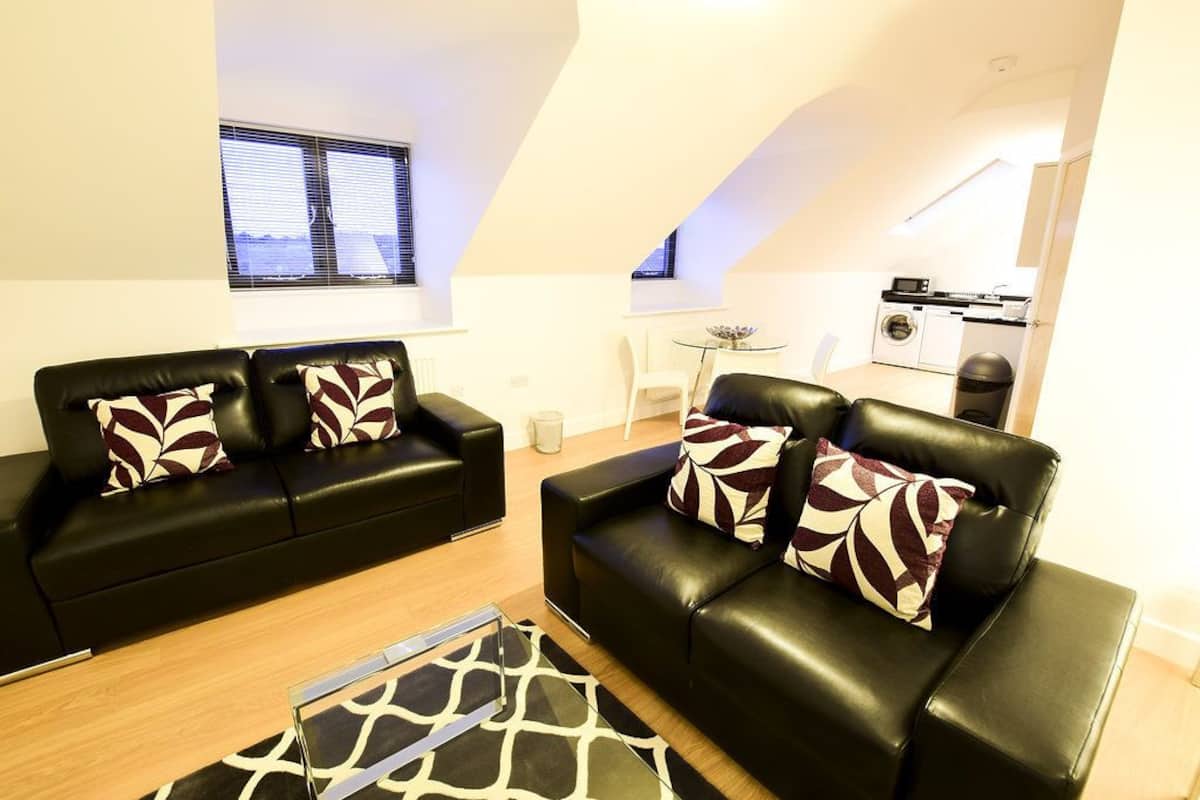 A modern living room with two black leather sofas, patterned cushions, a glass coffee table, and a giraffe-patterned rug.