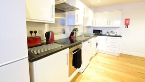 A modern kitchen with white cabinets, a black countertop, a red toaster, and a stainless steel range hood. - Roomspace Apartments -Kirk Court (Dorking)