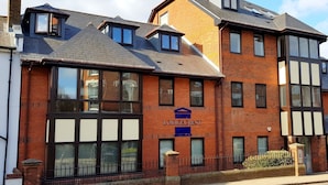 A brick building with a sign reading "Lodgecrest." It features multiple windows, a black metal fence, and a sloped roof. - Roomspace Apartments -Kirk Court (Dorking)