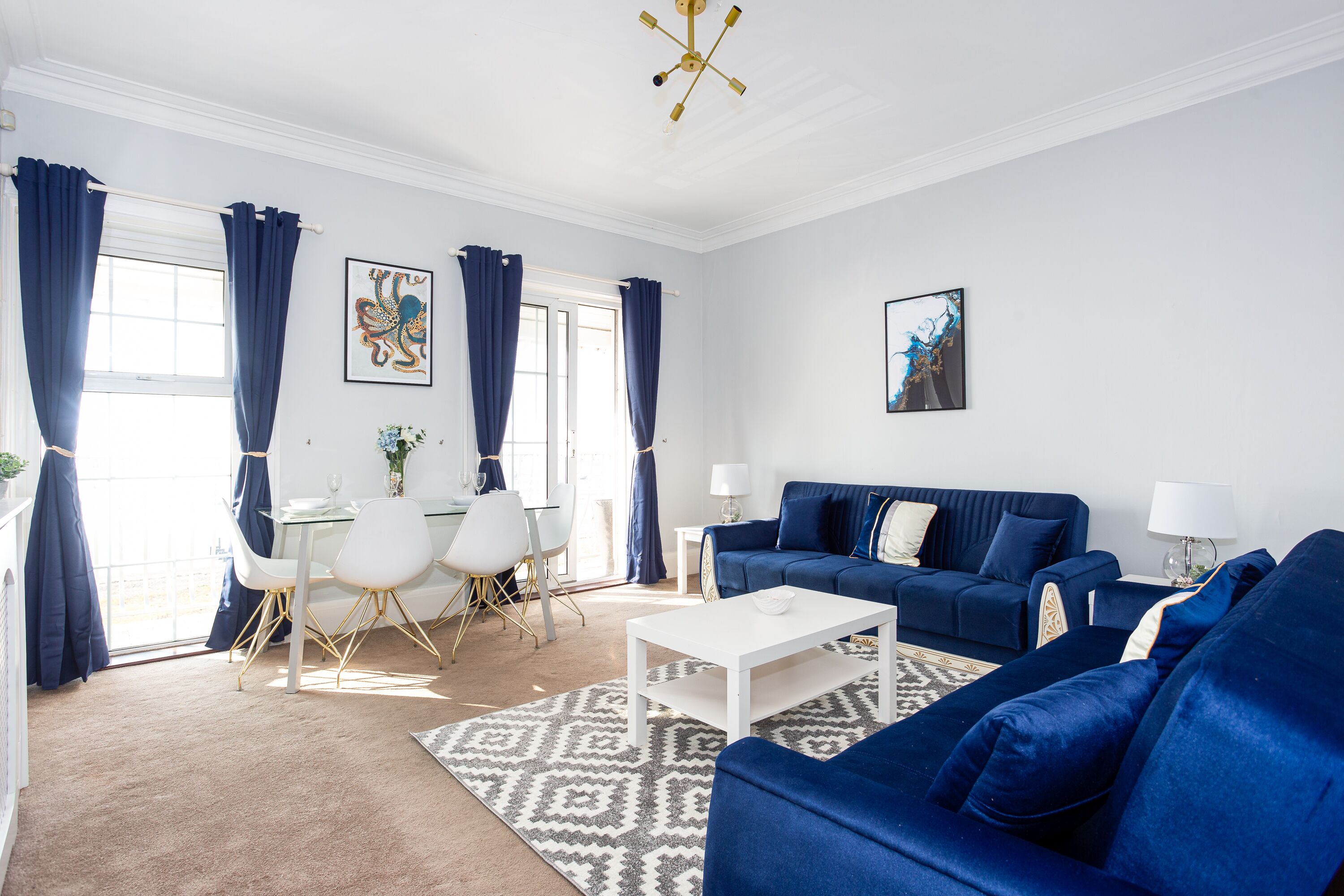 A modern living room with a blue sofa set, a white coffee table, and a dining area with a white table and chairs.