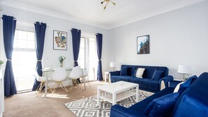 A modern living room with a blue sofa set, a white coffee table, and a dining area with a white table and chairs. - Compass Point by Sorted Stay  (Southend-on-Sea)
