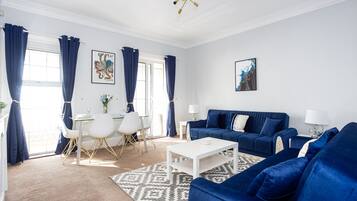 A modern living room with a blue sofa set, a white coffee table, and a dining area with a white table and chairs.