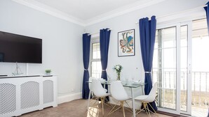A dining area with a glass table, white chairs, and a white console with a TV. - Compass Point by Sorted Stay  (Southend-on-Sea)