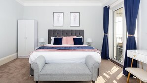 A bedroom with a bed, bedside tables, a bench, a wardrobe, and a window with curtains. - Compass Point by Sorted Stay  (Southend-on-Sea)