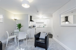A modern apartment with a dining area, a black leather chair, a kitchen, and a large mirror.