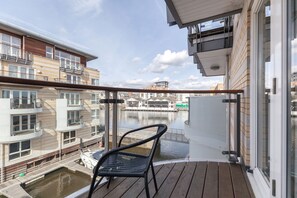 A balcony with a view of a canal, wooden deck, and a chair. - Roomspace Apartments -Marina Place (Kingston Upon Thames)
