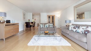 Uma sala de estar moderna com uma mesa de centro de vidro, um sofá cinza e um armário de madeira.