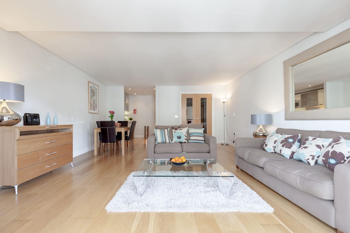 Ein modernes Wohnzimmer mit einem Glastisch, einem grauen Sofa und einem Holzkabinett.