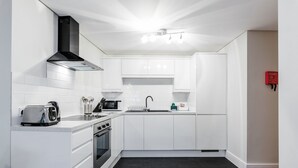 Uma cozinha moderna com armários brancos, um exaustor preto, uma torradeira, um micro-ondas e uma pia.