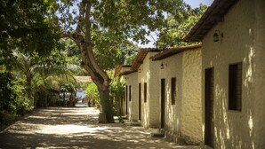 Una estrecha calle empedrada bordeada de edificios blancos con contraventanas marrones, que lleva a una vista distante de una masa de agua.