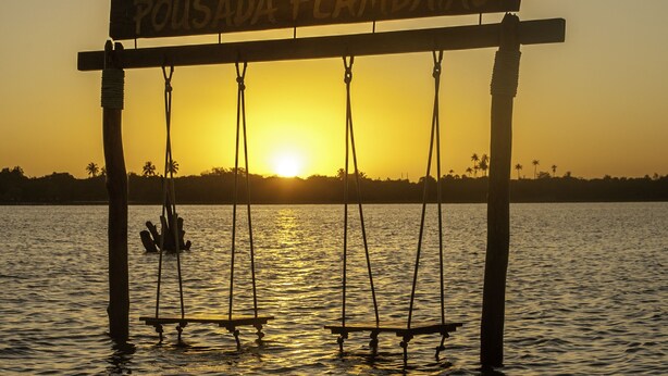 A wooden swing set over water with a sign that reads "Pousada Flambiao".