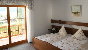 Una camera da letto con un letto di legno, biancheria da letto floreale, un comodino, un quadro e una porta scorrevole in vetro che dà su un balcone.