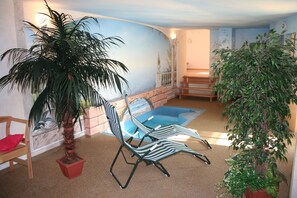 Une pièce avec une piscine, deux chaises longues, une chaise en bois et deux plantes en pot.