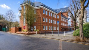 A multi-story brick building with a bike-sharing station sign, a "Book Space" sign, and a clear blue sky. - Roomspace Apartments -Nouvelle House (Sutton)