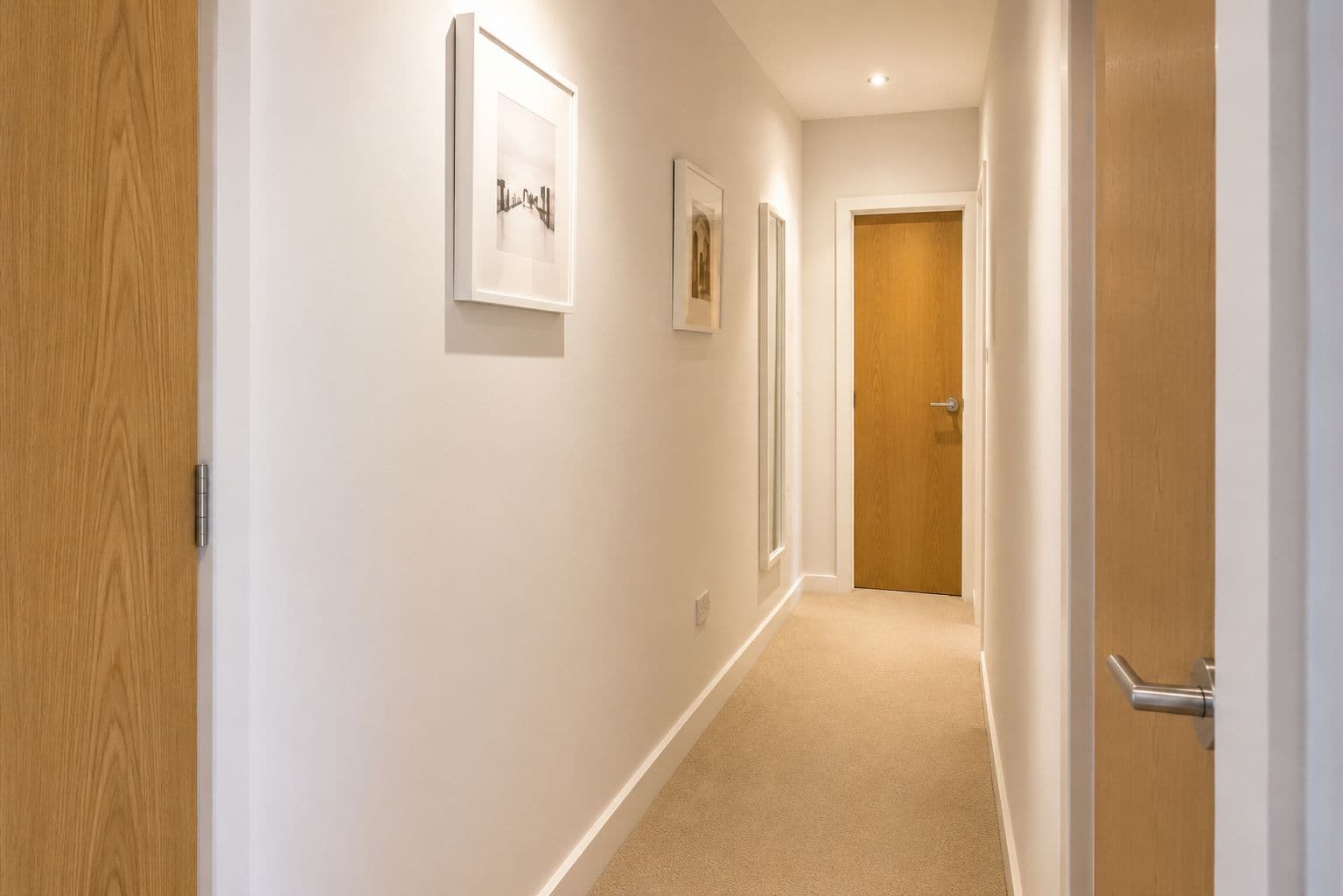 A hallway with wooden doors, white walls, and framed pictures on the wall.