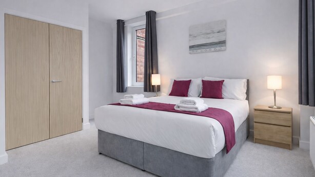 A modern hotel room with a large bed, two bedside tables, a wardrobe, and a window with curtains. - Roomspace Apartments -Nouvelle House (Sutton)