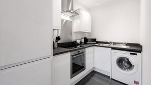 A compact kitchen with a built-in oven, microwave, and washing machine. - Roomspace Apartments -Nouvelle House (Sutton)