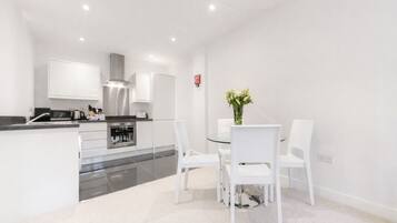 A modern kitchen with white cabinetry, a stainless steel range hood, and a dining area with a glass table and white chairs.