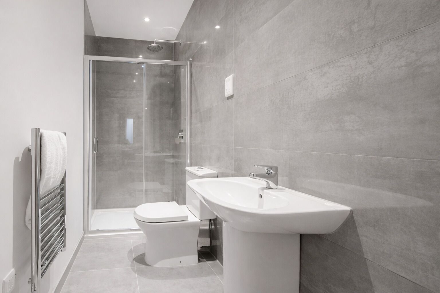 A modern bathroom with a glass-enclosed shower, a white sink, and a toilet.