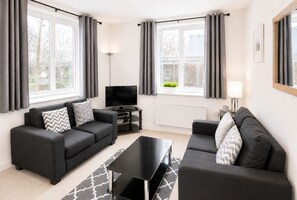A modern living room with two black sofas, a black coffee table, a flat-screen TV, and a radiator.
