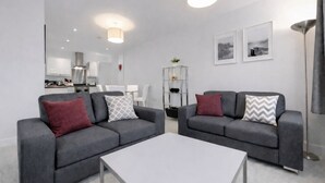 A modern living room with two grey sofas, a white coffee table, and a dining area in the background. - Roomspace Apartments -Nouvelle House (Sutton)