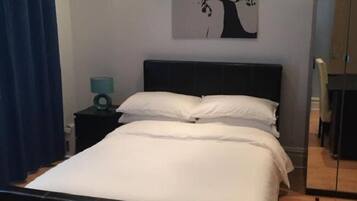Una cama bien hecha con sábanas blancas, un cabecero oscuro y una mesita de noche con una lámpara.