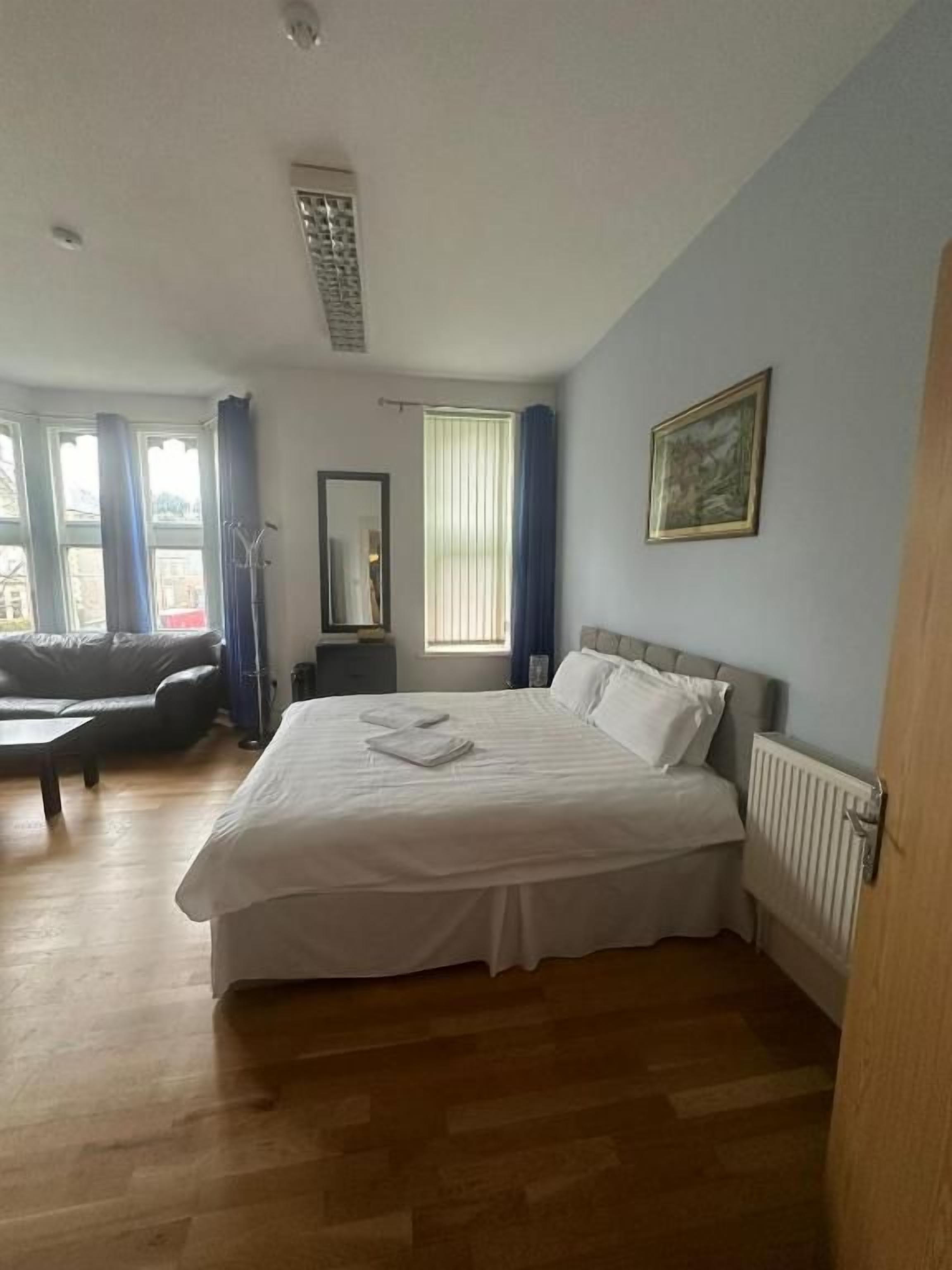 A bedroom with a large bed, a window with curtains, a radiator, and a painting on the wall.