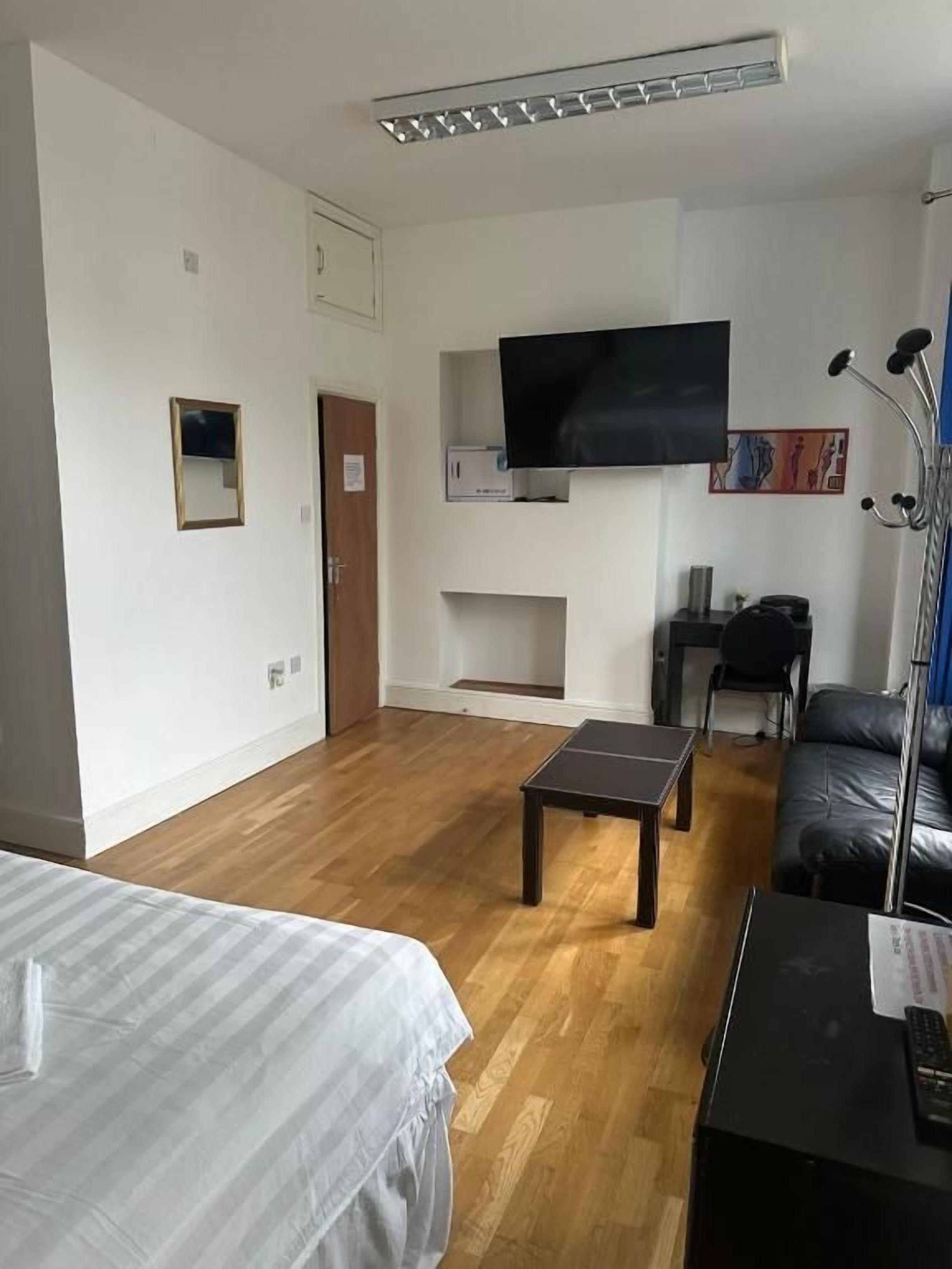 Hotellihuone, jossa on sänky, työpöytä, tuoli, seinälle asennettu taulutelevisio ja puulattia.
