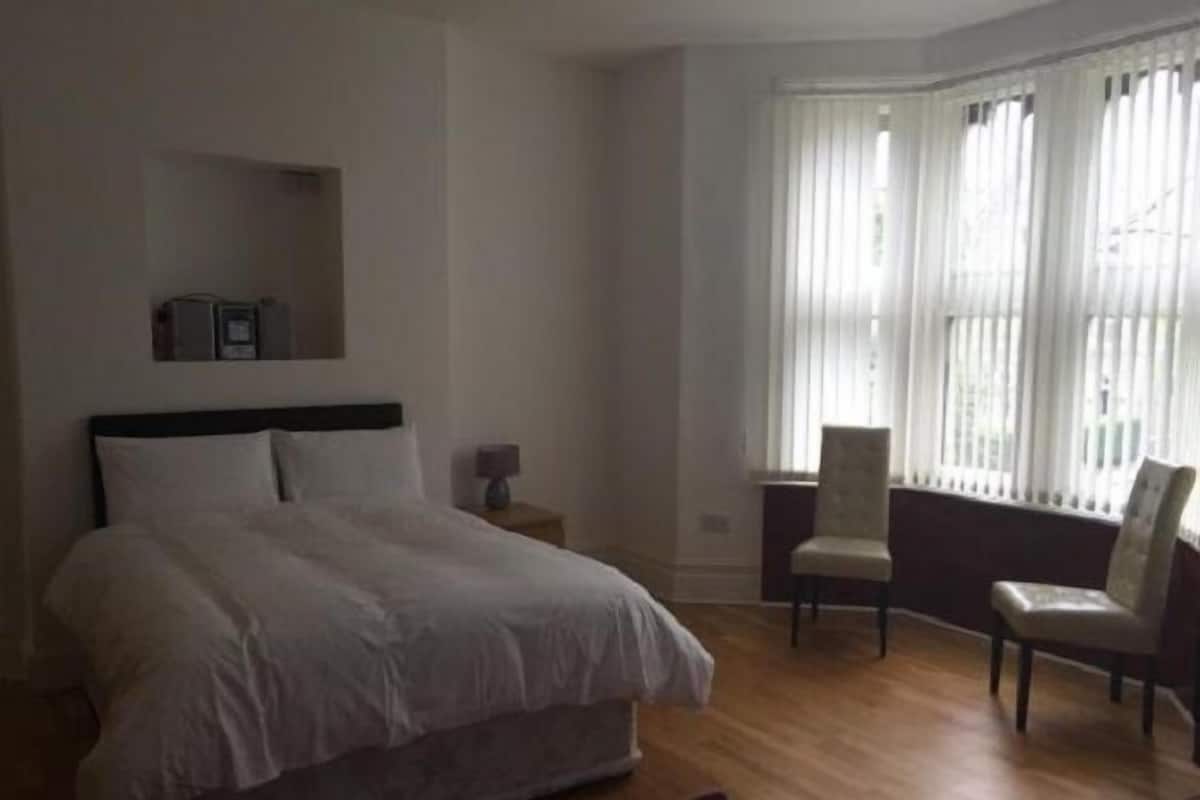 Een slaapkamer met een bed, een nachtkastje, een stoel en een raam met gordijnen.