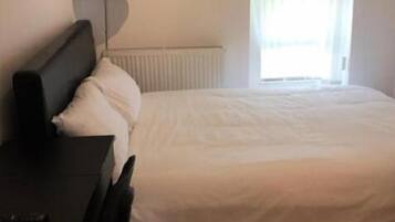 A bedroom with a bed, a desk, a chair, a lamp, and a window with curtains.