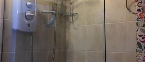 A glass-enclosed shower stall with a handheld showerhead, a wall-mounted control panel, and a shower caddy.
