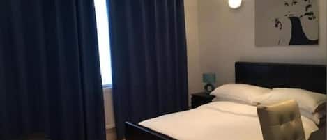 A hotel room with a bed, a nightstand, a chair, and a painting on the wall.
