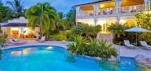 A pool area with lounge chairs, a two-story building with a balcony, and tropical landscaping.