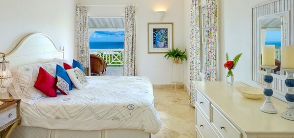A bedroom with a bed, a dresser, a mirror, a potted plant, and a view of the sea through a door.