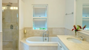 Un baño con bañera, ducha, lavabo y ventana con persianas.