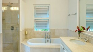 Ein Badezimmer mit einer Badewanne, einer Dusche, einem Waschbecken und einem Fenster mit Jalousien.