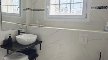 Une salle de bain moderne avec un lavabo blanc, un porte-serviettes noir et une fenêtre ornée d’une bordure de carreaux décoratifs.